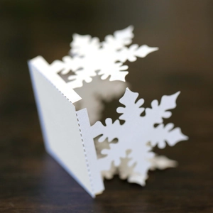Detailed macro view of laser-cut white snowflake card with intricate hollow pattern