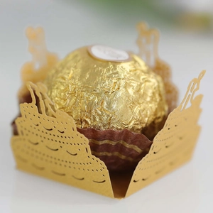 Macro shot of gold laser-cut paper cupcake wrapper with intricate hollow birthday cake design
