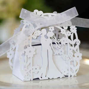 Close-up of laser-cut white wedding favor box with romantic silhouette and organza ribbon