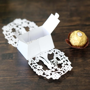 Detail of white laser-cut wedding candy box with floral patterns on wooden background