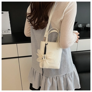 Detail of white bucket bag with floral charm and adjustable strap shown on model