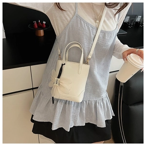 Close-up of a white bucket bag with floral charm and long shoulder strap on model