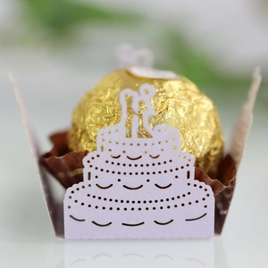 Close-up of laser-cut wedding cake paper holder with golden chocolate on white desk