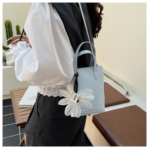 Detail of light blue mini bucket bag featuring a large white fabric flower charm accessory