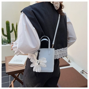 Detail of light blue bucket bag with white floral pendant and fashion stamp