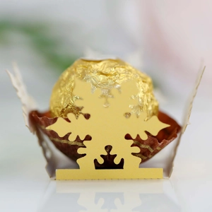 Macro view of a gold hollow snowflake-themed paper chocolate holder and festive box