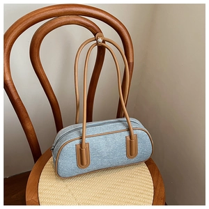 Detail of light blue denim Boston bag with brown leather straps on a vintage chair