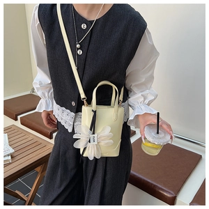 Detail of a light yellow bucket bag featuring a large mesh flower charm in a cafe setting