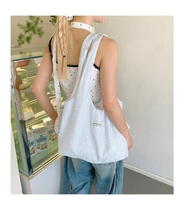 Detailed side view of light blue floral canvas tote bag carried by a model in a cafe
