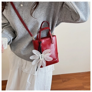 Detail of red mini bucket bag with a large white daisy charm and thin leather strap