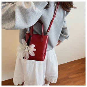 Detail of red glossy bucket bag with 3D white flower charm and FUOR ribbon strap