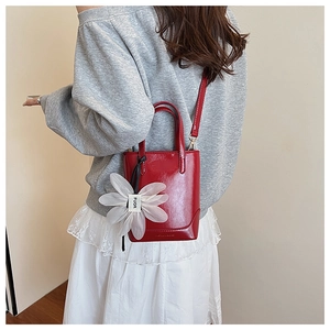 Detail view of red glossy mini bucket bag with white floral charm and logo embossing