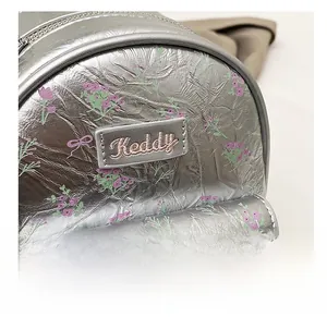 Close-up of silver backpack detail featuring floral print and Keddy embroidered label