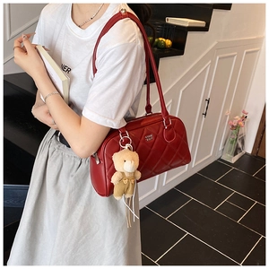 Sac bandoulière rouge matelassé avec bijou d'ours et logo doré porté par un modèle