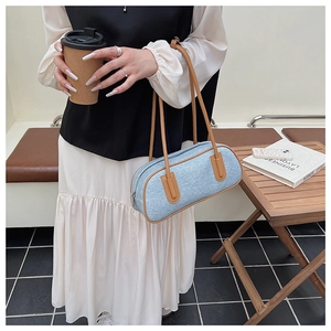 Dettaglio della borsa a cilindro in denim azzurro con cinturini in pelle marrone e zip
