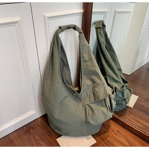 Detail of olive green nylon tote bag featuring front flap pocket and drawstring side pocket