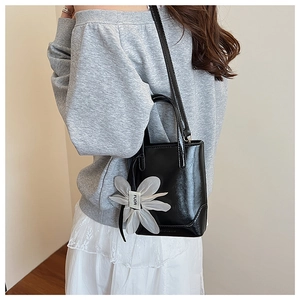 Detail of black patent leather bucket bag with white floral pendant on a female model