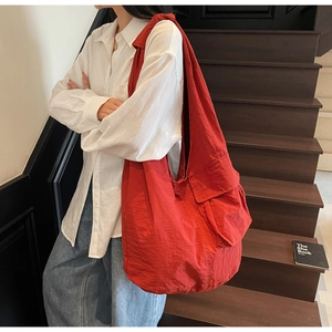 Red high-capacity nylon tote bag with side flap pocket worn by model in casual style