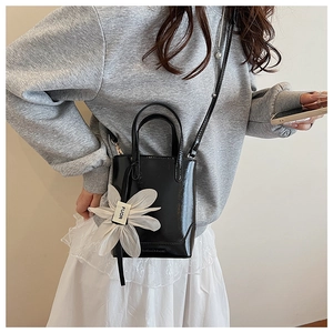 Close-up of black patent leather bucket bag with white lace daisy charm and slim strap