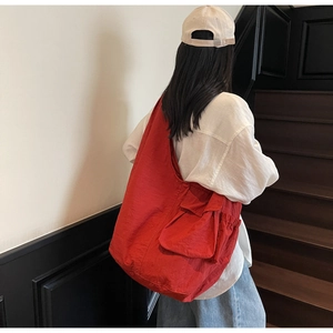 Detail view of a large red nylon shoulder bag with side drawstring pockets on a model