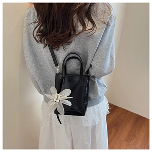 Detail of black glossy bucket bag featuring a white fabric flower charm and leather texture