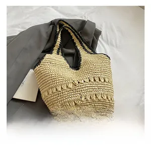 Detail showing woven texture and hollow design on a straw tote bag with black contrast straps