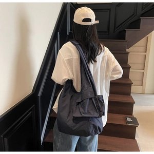 Detail of dark blue oversized tote bag with knot strap on a textured nylon shoulder bag