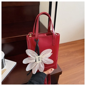 Detail of red patent leather bucket bag with a white floral charm on a wooden background