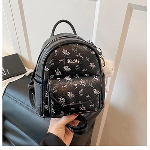 Dettaglio mini zaino nero con stampe floreali e fiocchi con ciondolo a pompon bianco