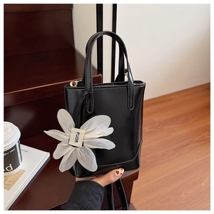 Detail of black glossy bucket bag with delicate white floral charm and logo