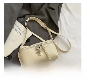 Detail of cream mini crossbody bag featuring a unique silver metal robot pendant charm