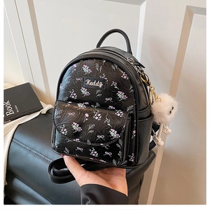 Dettaglio dello zaino nero con stampe floreali viola e ciondolo di peluche bianco