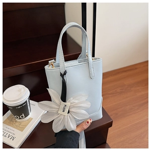 Detail of light blue mini bucket bag with white flower charm on a red wooden step