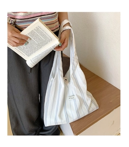 Detail of blue striped canvas tote bag with woven label held in a minimalist setting