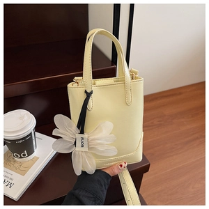 Detail of cream leather bucket bag with top handles and a decorative 3D floral charm