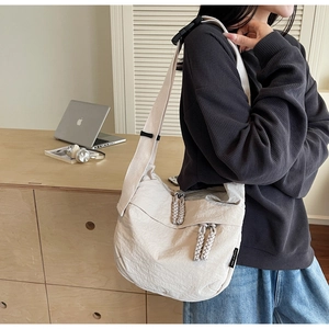 Close-up of beige pleated nylon crossbody bag with wide strap and branded tag detail