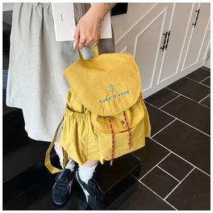 Détail d'un sac à dos en nylon jaune avec broderie bleue et poche latérale sur un mannequin