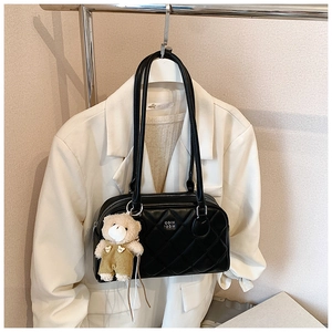 Détail d'un sac à bandoulière matelassé noir avec pendentif ours sur blazer blanc