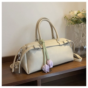 Close-up of beige lychee leather Boston bag with a purple tulip charm on wood shelf