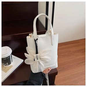 Close-up of a white mini leather bucket bag featuring a large white fabric flower charm