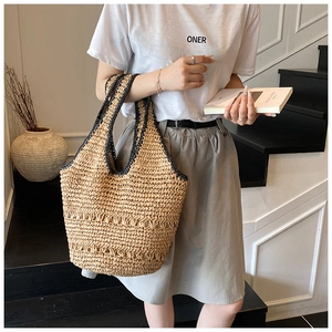Detail of hand-woven straw tote bag with black contrast stitching in lifestyle setting