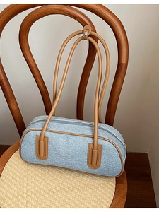 Borsa a cuscino in denim azzurro con manici in pelle marrone appesa a una sedia in legno
