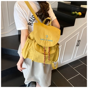 Détail d'un sac à dos jaune gingembre avec broderie bleue et poche latérale élastique
