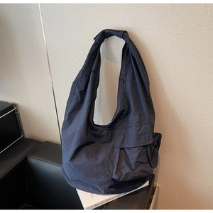 Detail of navy blue oversized tote bag featuring a front flap pocket and knot shoulder strap
