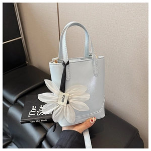 Detail of light blue bucket bag with white daisy charm and adjustable strap on leather seat