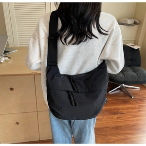 Detail of black crescent canvas bag showing zip closure and woven brand tag on shoulder strap