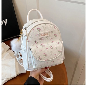 Primo piano di un mini zaino bianco con motivi floreali rosa e un ciondolo a pompon