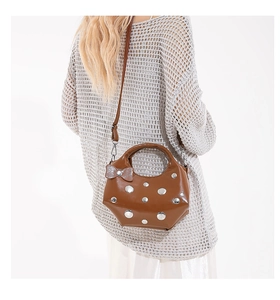 Detail of brown glossy crescent bag with silver rivets and bow charm worn by a model