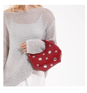 Détail d'un sac à bandoulière en cuir verni rouge avec clous métalliques sur un modèle