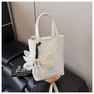 Detail of white leather bucket bag with a delicate floral charm and adjustable shoulder strap